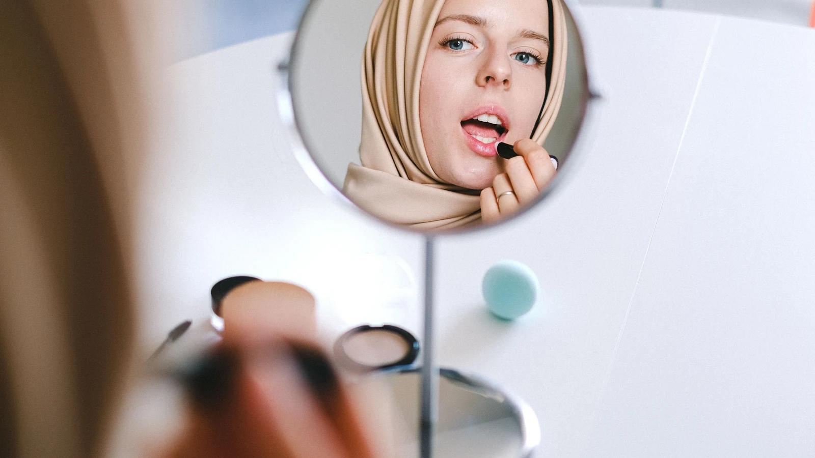 زن محجبه در حال زدن رژ لب مقابل آینه گرد